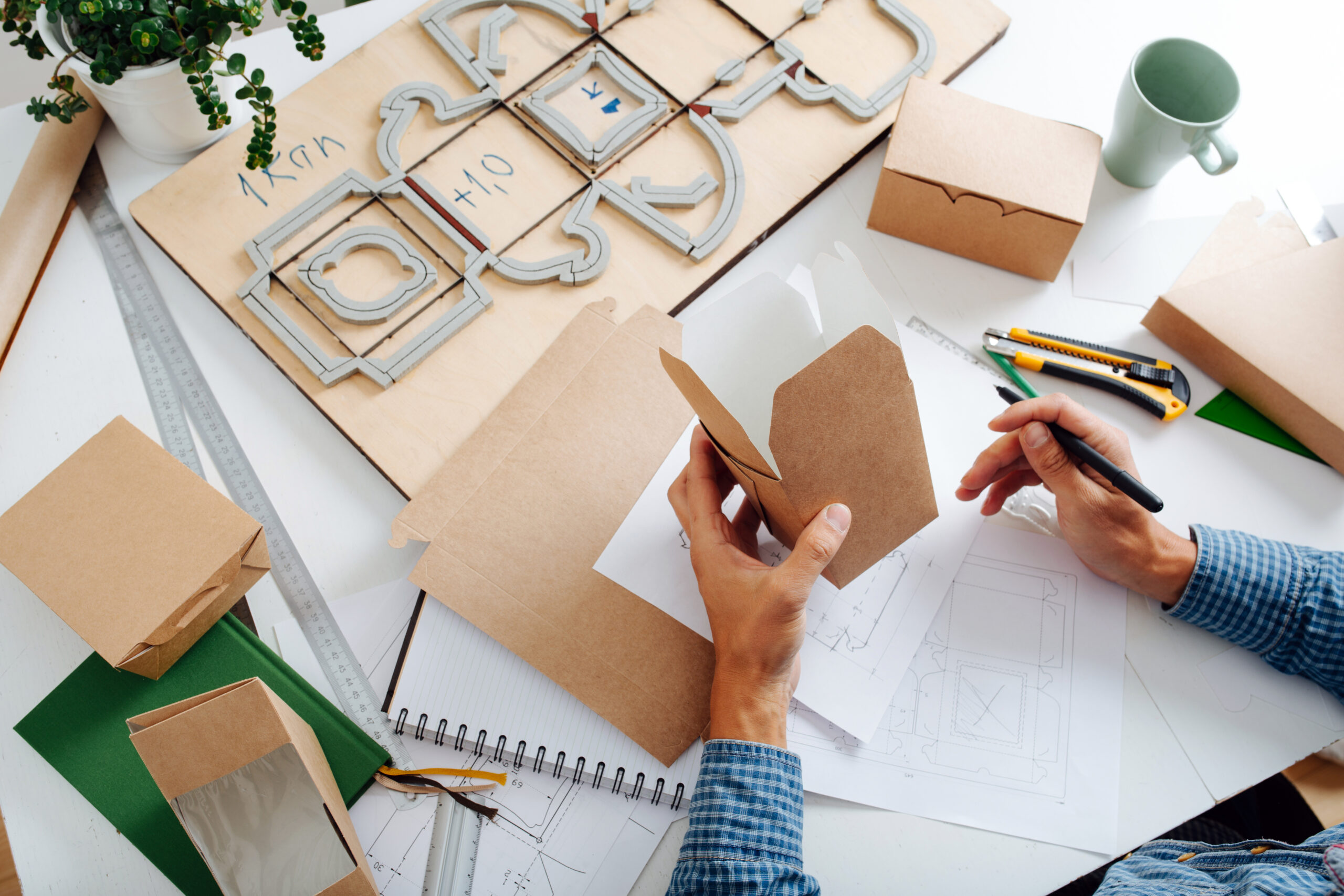 Hands holding a box in hands, thinking process on ways to improve it. Sitting behind the desk. No face. High angle.